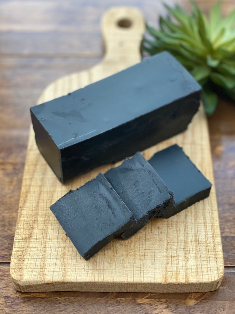Three slices of liquorice fudge on a wooden cutting board with a plant in the background.