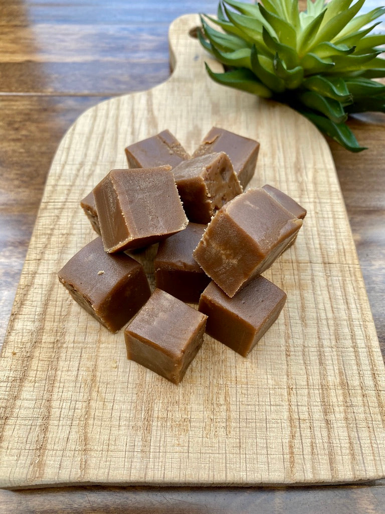 Cubes of chocolate fudge on a wooden cutting board with a plant in the background