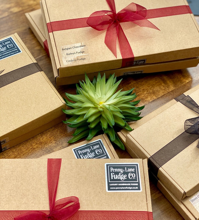 Gift-wrapped handmade fudge boxes from Penny Lane Fudge Co with black and burgundy ribbon on a wooden surface.