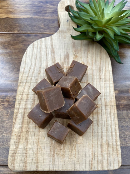 Chocolate fudge pieces on a wooden cutting board with a plant in the background
