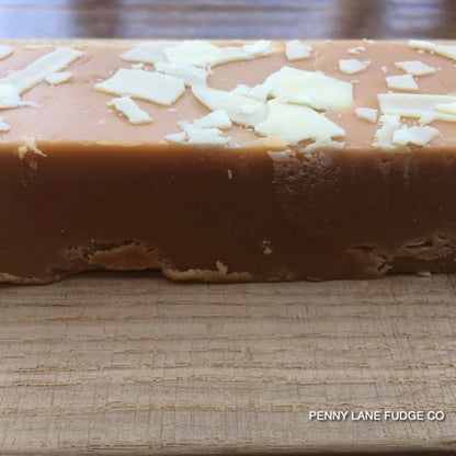Block of fudge with white chocolate shavings on a wooden surface, branded 'Penny Lane Fudge Co'.