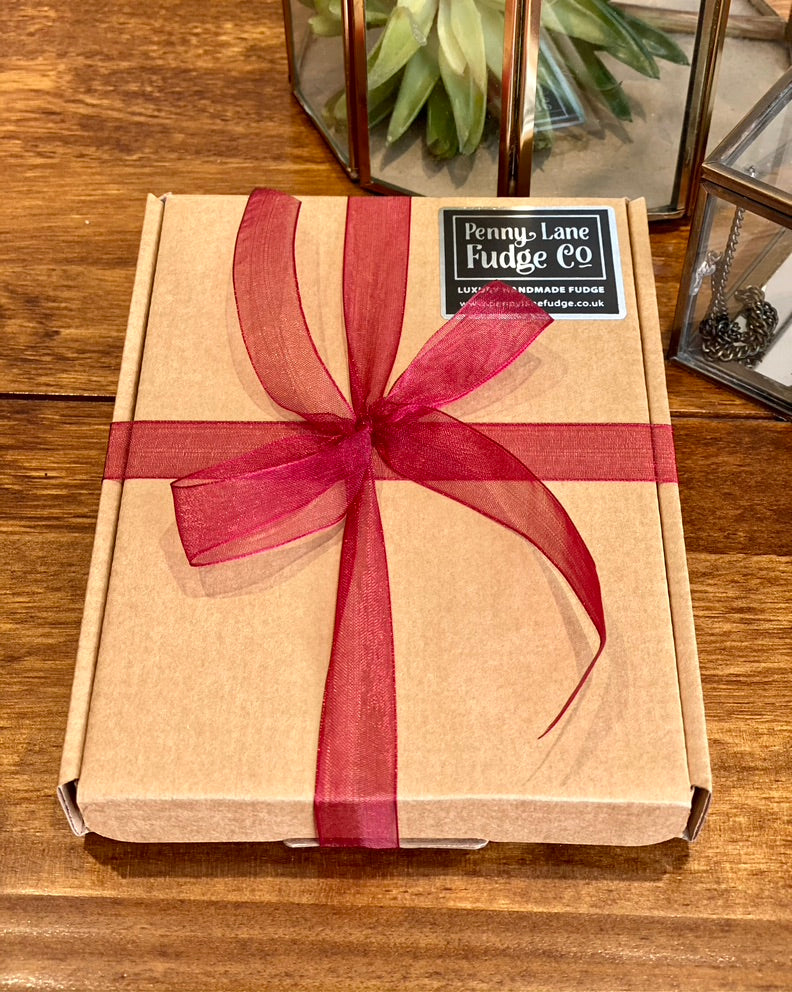 Box of Penny Lane Fudge Co. wrapped with a red ribbon on a wooden surface.