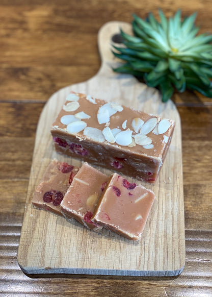 a bar and slices of cherry and almond fudge, topped with chopped almonds and pieces of dried cherry, arranged on a wooden chopping board