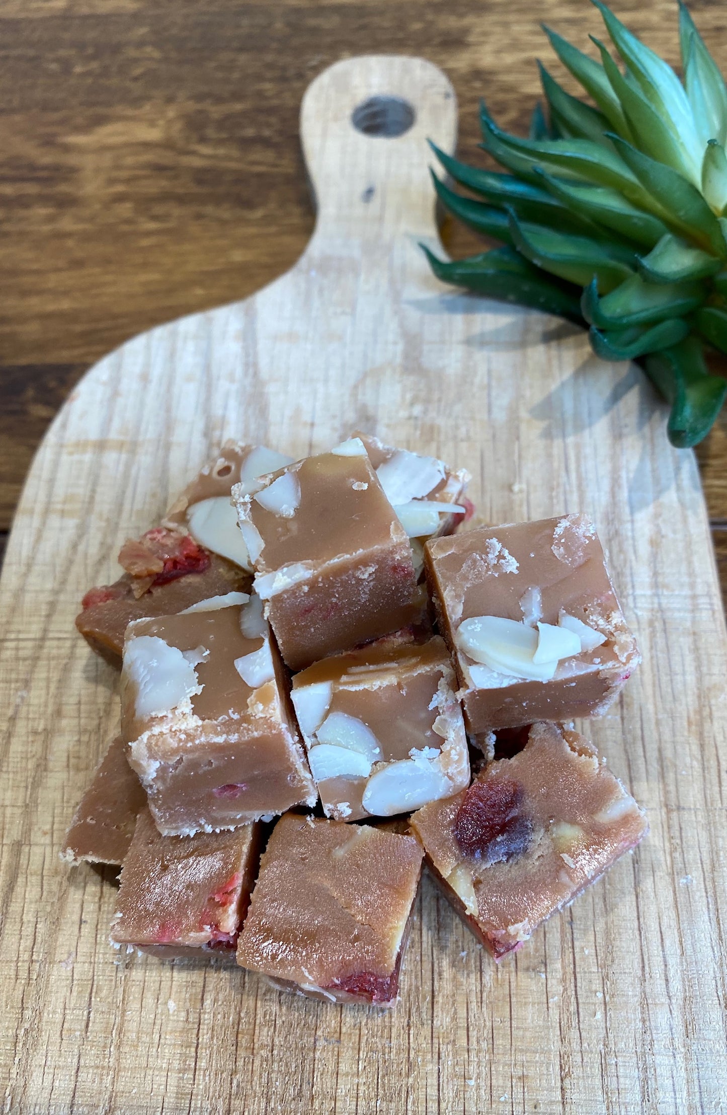 cubes of cheery and almond fudge on a wooden cutting board with a plant in the background