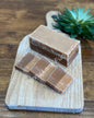 Three pieces of coffee and cream fudge on a wooden board with a plant in the background