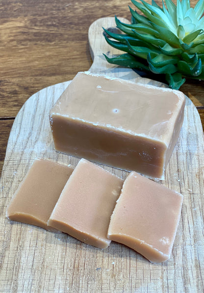 Three slices of creamy fudge on a wooden cutting board with a plant in the background.