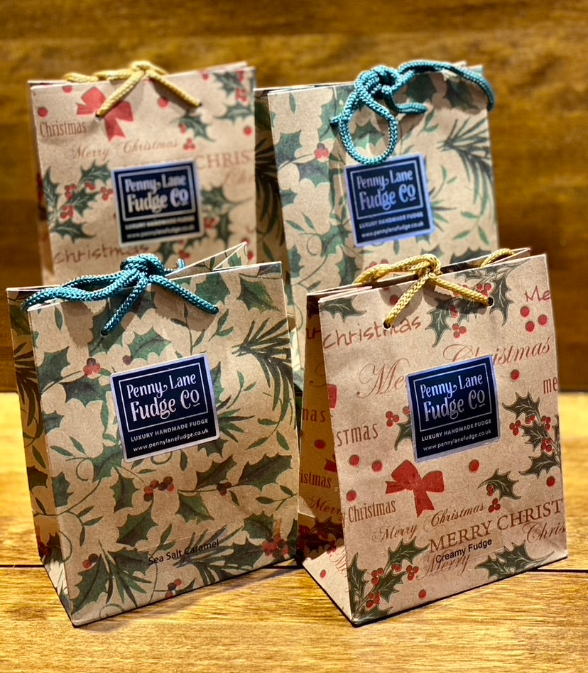 Four small Christmas-themed gift bags with 'Penny Lane Fudge Co' label on a wooden surface.