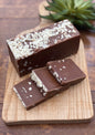 Belgian Chocolate bar with white choclate shavings topping on a wooden cutting board with a plant in the background