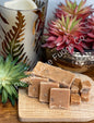 Square pieces of fudge on a wooden board with succulents and a candle in the background.