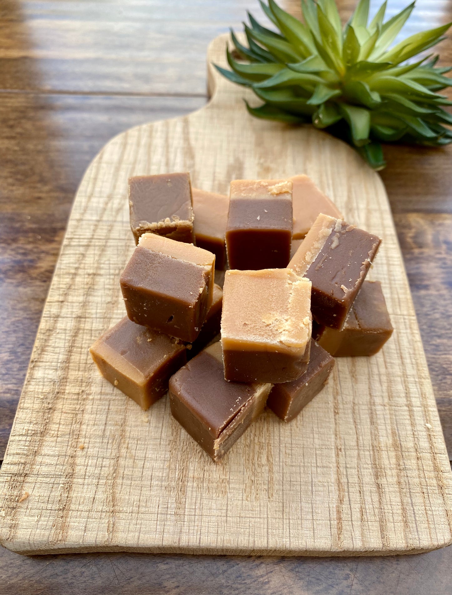 Cubes of millionaire fudge on a wooden cutting board with a plant in the background