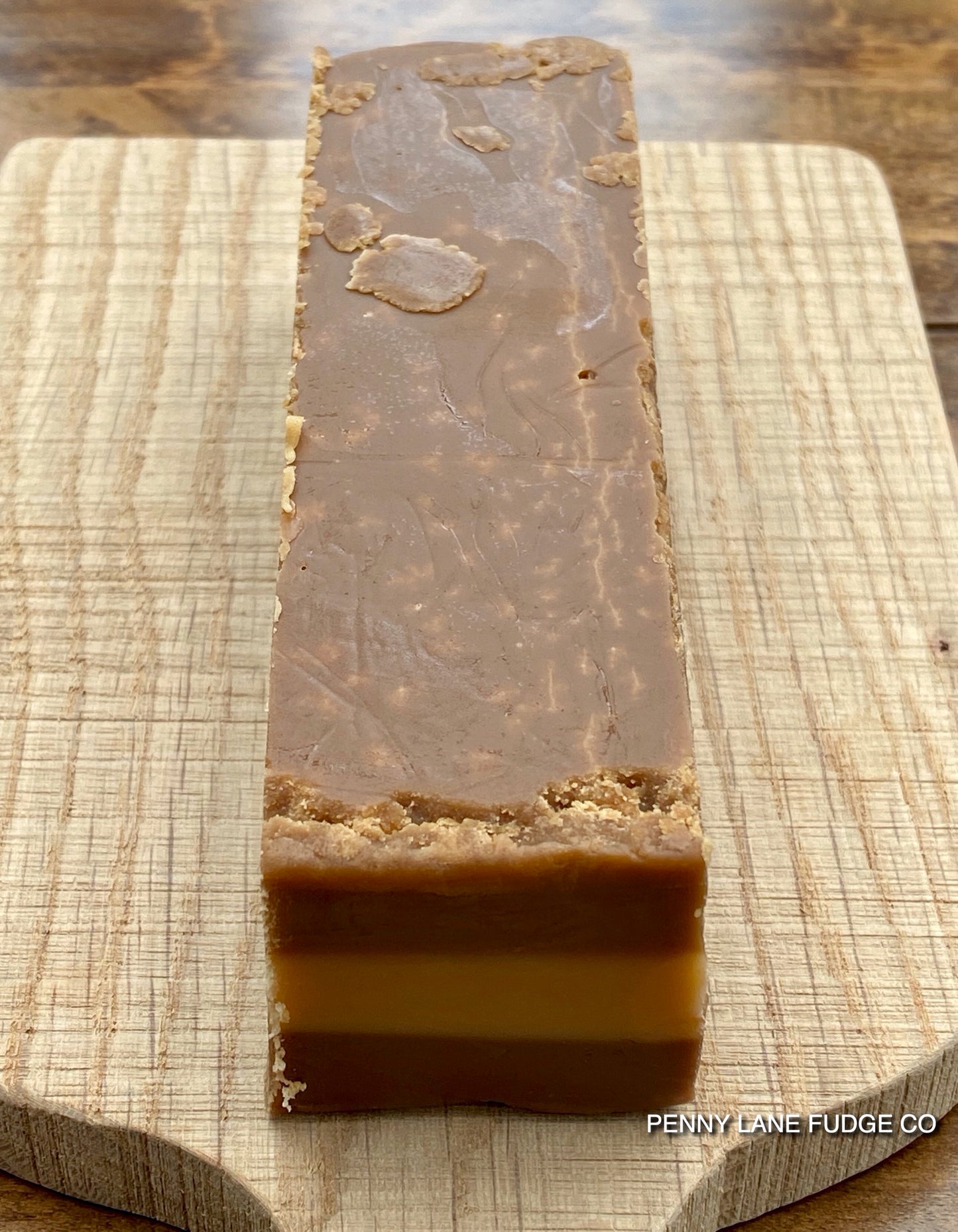 tri coloured block of millionaire fudge on a wooden cutting board with 'Penny Lane Fudge Co' branding.