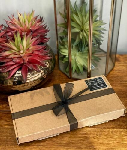 Gift box with a black ribbon on a wooden surface with plants in the background