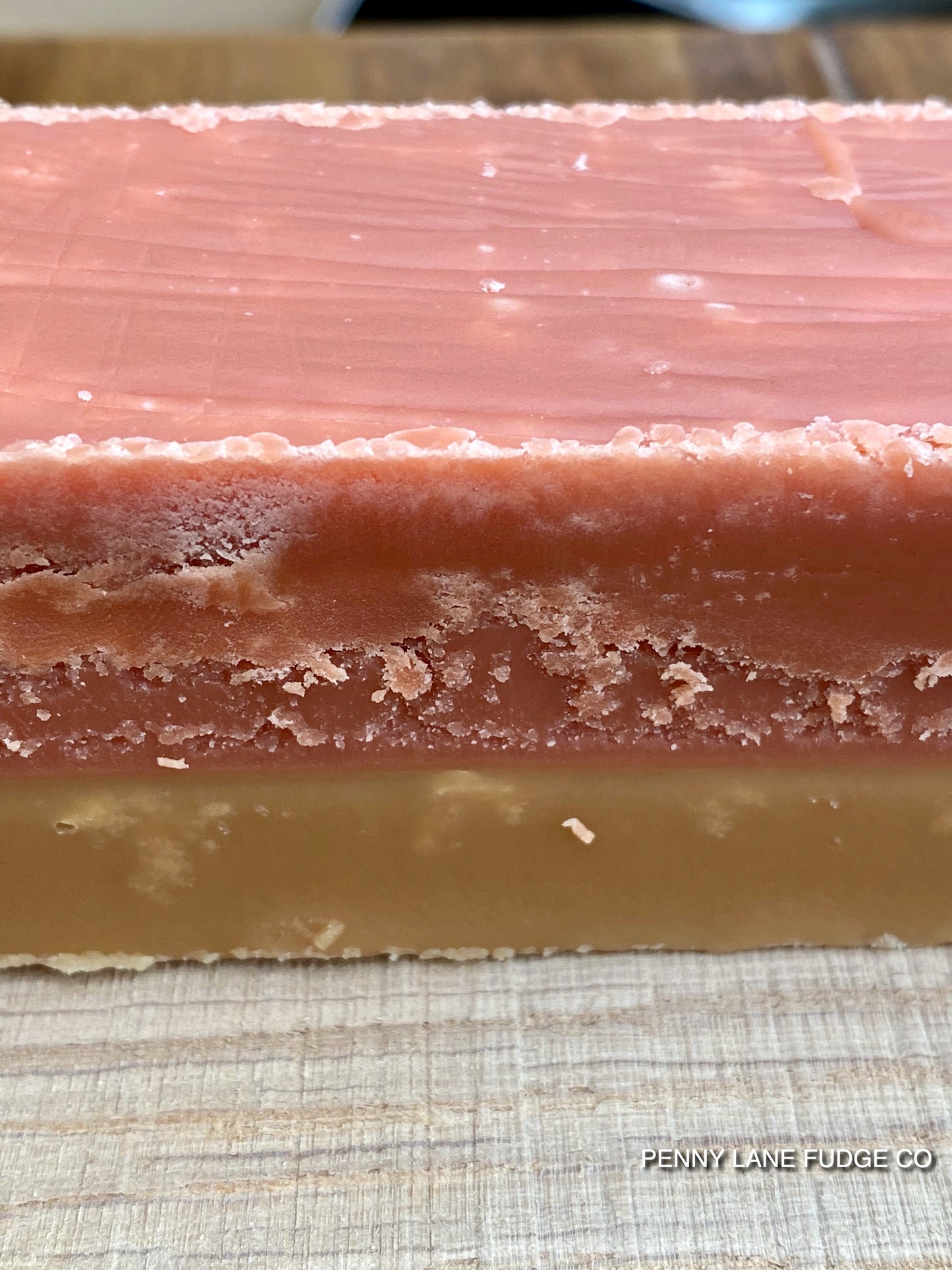 Close-up of a layered fudge bar of sgtrawberry and cream fudge with 'Penny Lane Fudge Co' branding.