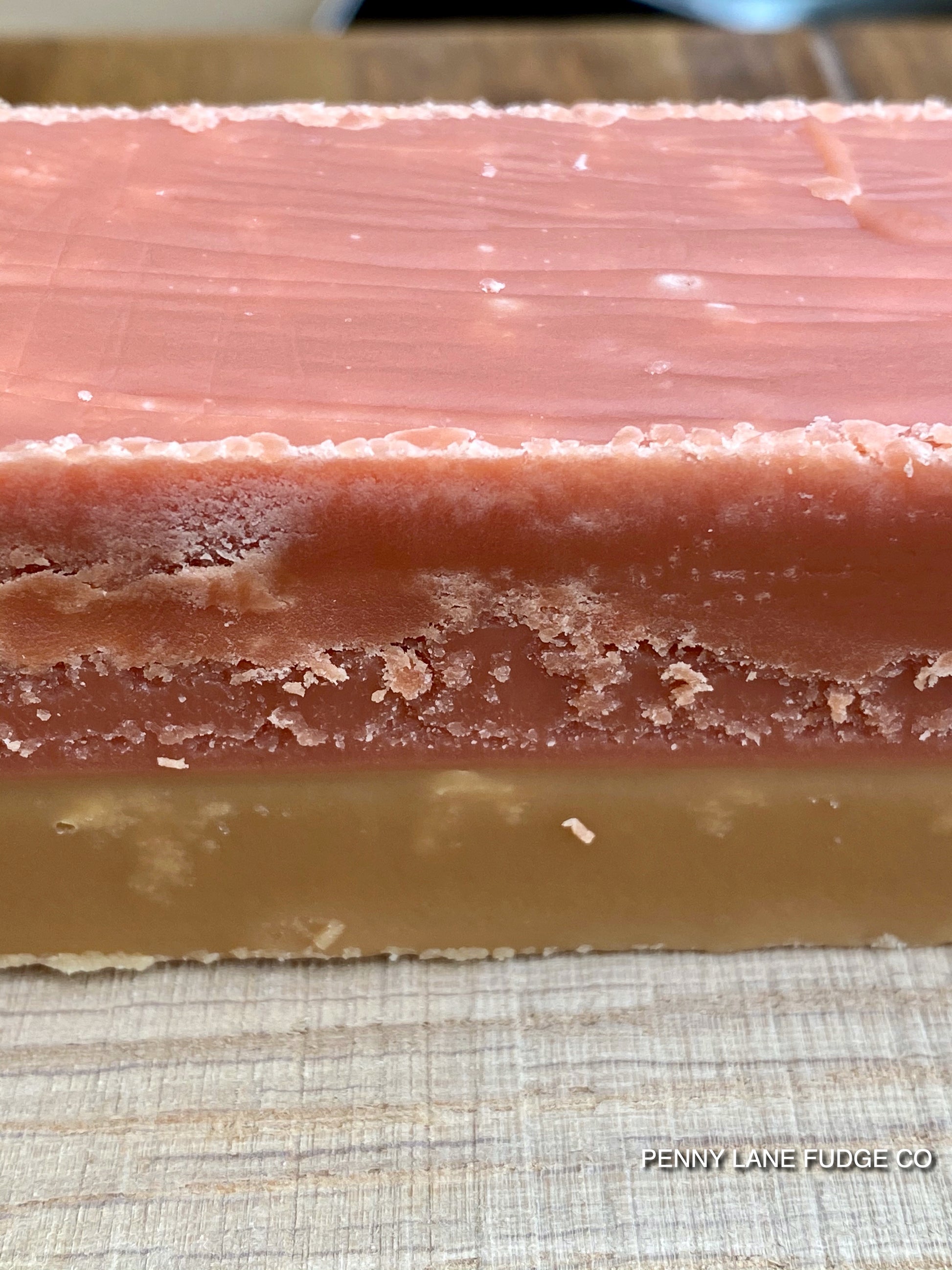 Close-up of a layered fudge bar of sgtrawberry and cream fudge with 'Penny Lane Fudge Co' branding.