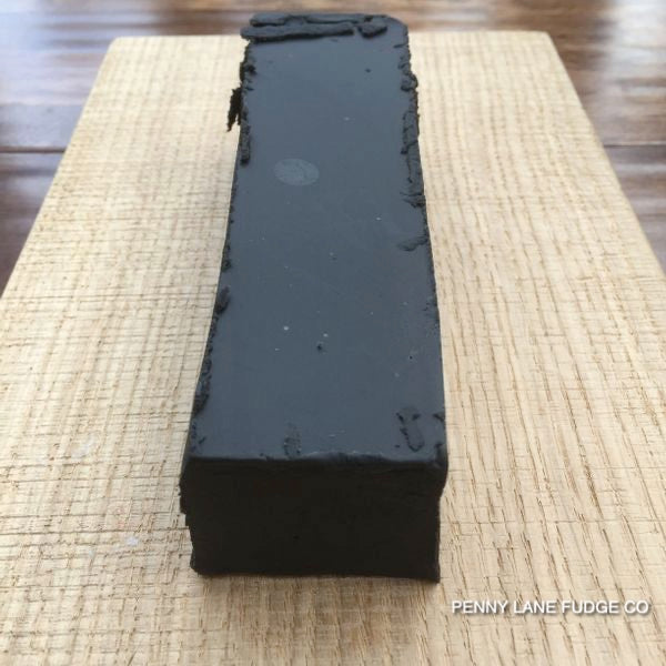 Block of black liquorice fudge on a wovoden surface with 'Penny Lane Fudge Co' branding.