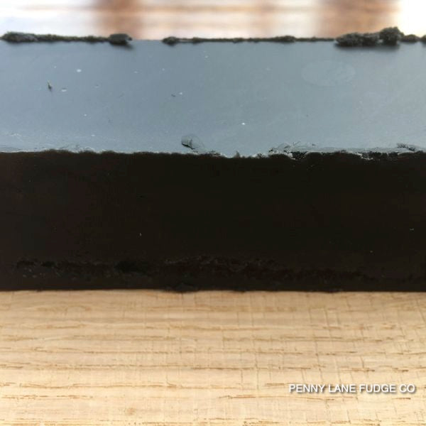 Close-up of a block of black liquorice fudge on a wooden surface with 'Penny Lane Fudge Co' branding.