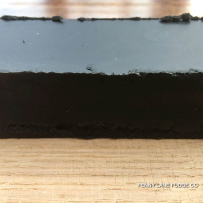 Close-up of a block of black liquorice fudge on a wooden surface with 'Penny Lane Fudge Co' branding.