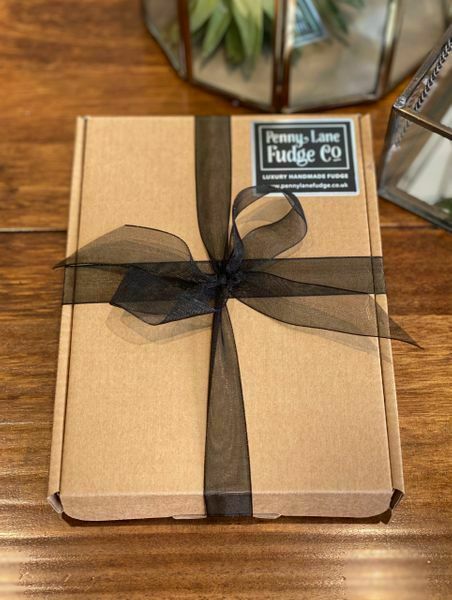 Kraft paper box with a black ribbon and 'Penny Lane Fudge Co' label on a wooden surface.