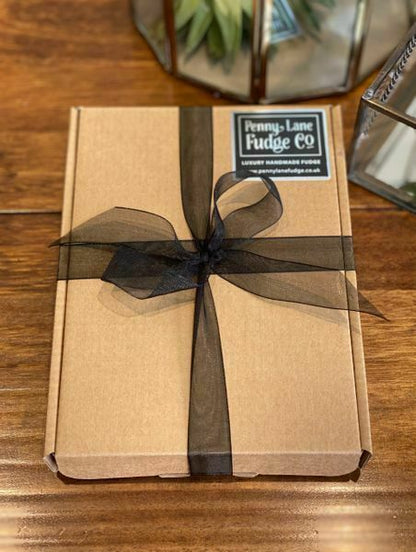 Kraft paper box with a black ribbon and 'Penny Lane Fudge Co' label on a wooden surface.